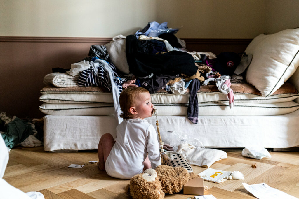 petite fille assise par terre dans la chambre devant un monticule de vêtements