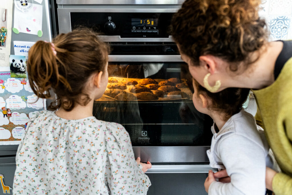deux petites filles et leur maman regardant les cookies cuire dans le four
